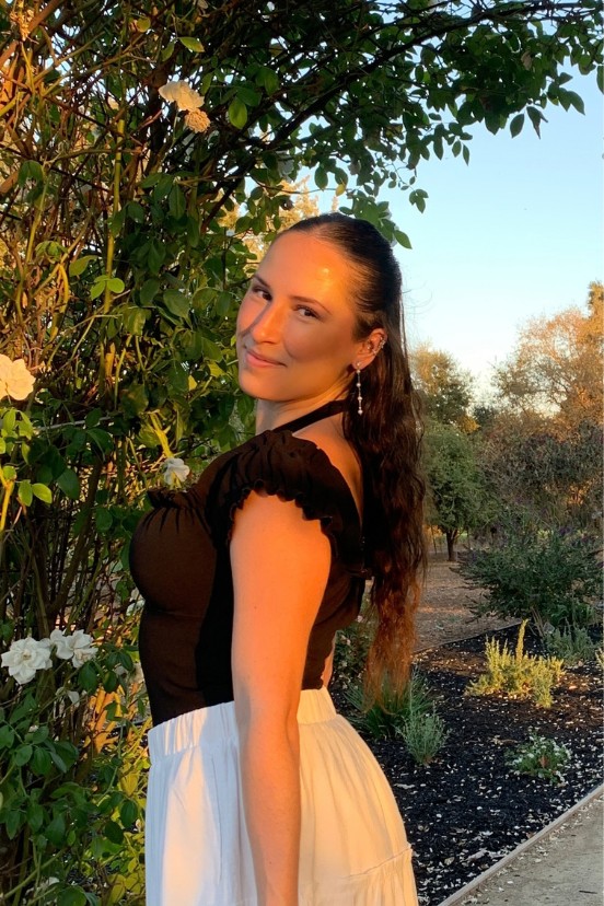 Jenny Hobbs smiling over her shoulder in a garden at sunset
